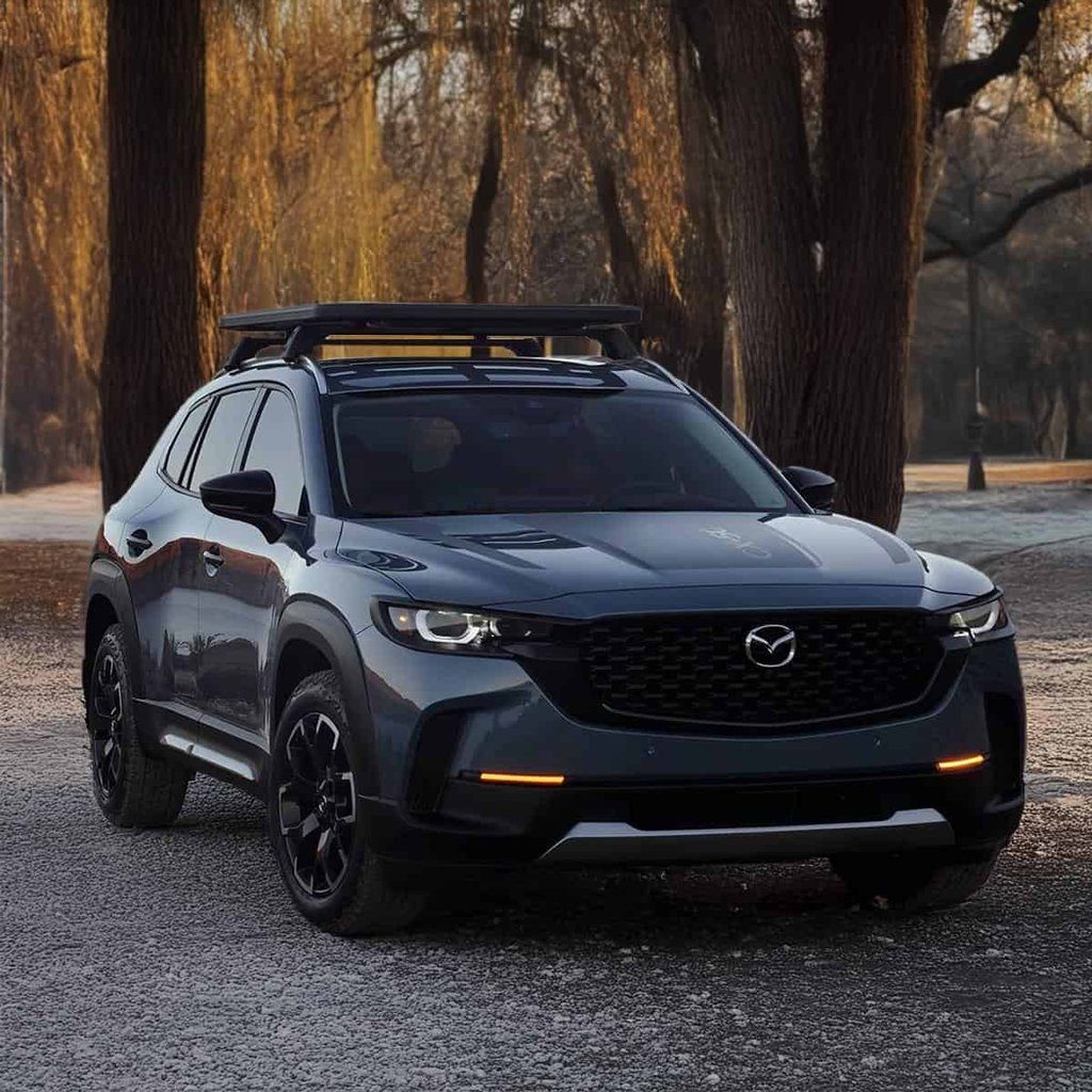 The Mazda CX-50 showcasing its wide, aggressive stance and signature black plastic body cladding on a gravel mountain pass.